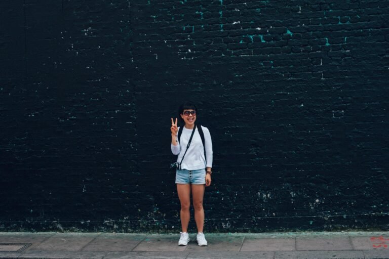 Effective Blog Promotion: Strategies to Increase Your Reach Smiling woman in sunglasses, posing with a peace sign against a brick wall.